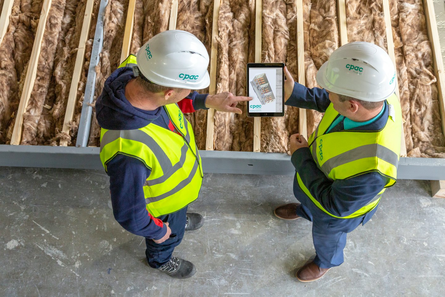 Dvaja stavební robotníci si prezerajú digitálny tablet na stavenisku.